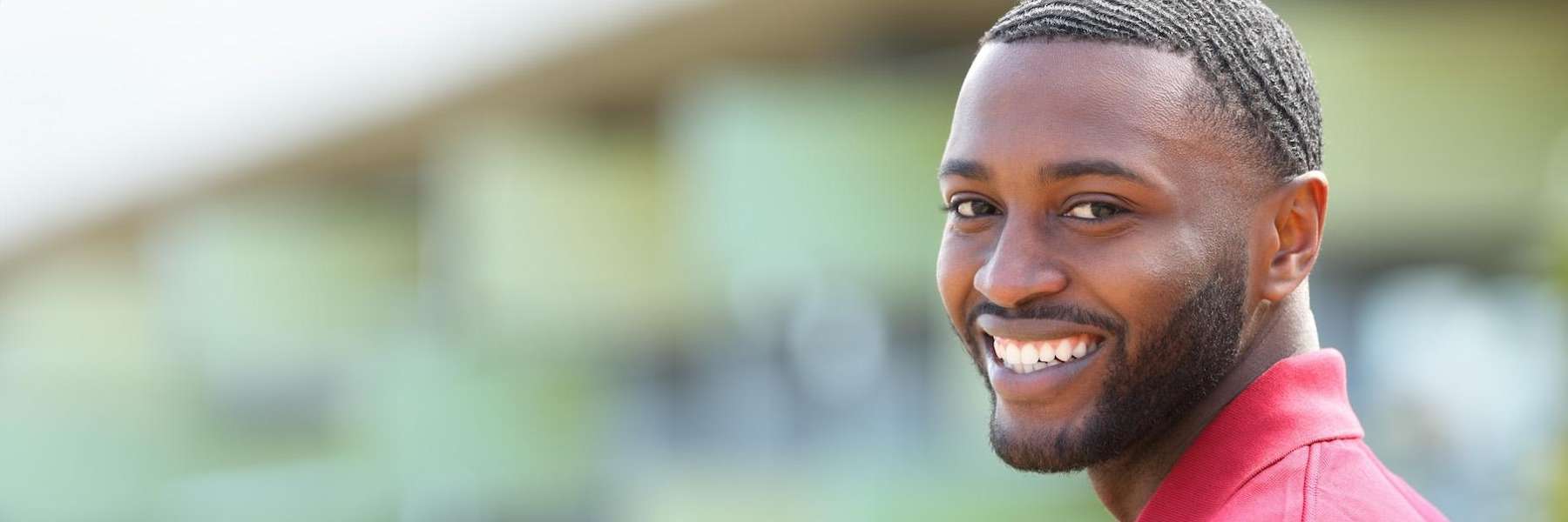 A man in a red shirt smiles at the camera, promoting dental implant care tips in Bellevue, NE.