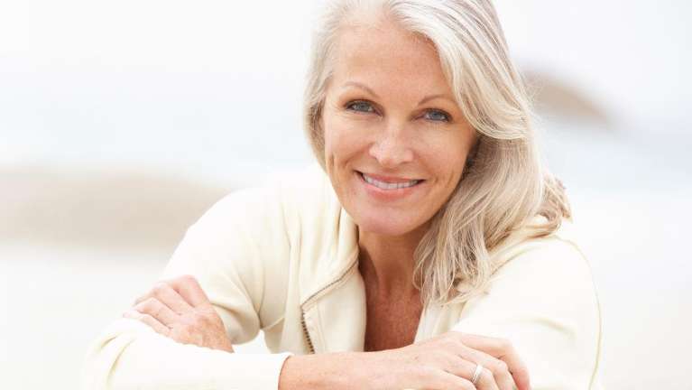White-haired woman smiles slightly while wearing her front dental implant in Nebraska