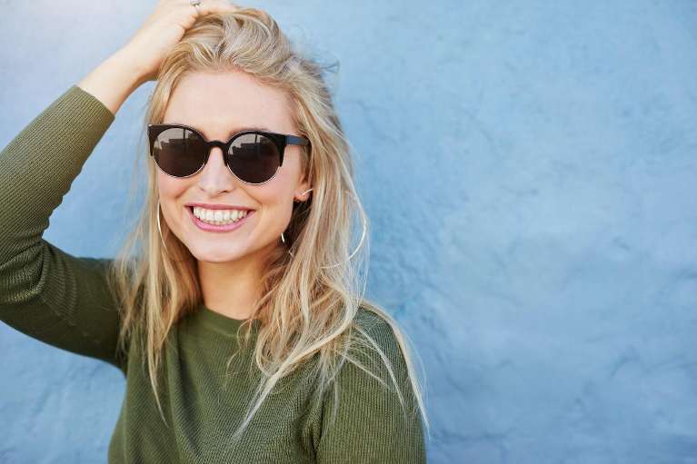 A confident woman smiling in sunglasses after choosing Invisalign® over braces.