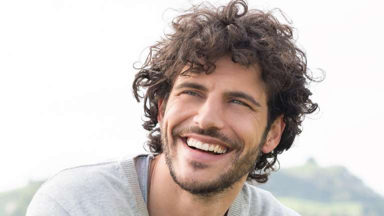 1. A man with curly hair smiles, emphasizing the importance of preventive dental care for long-term.